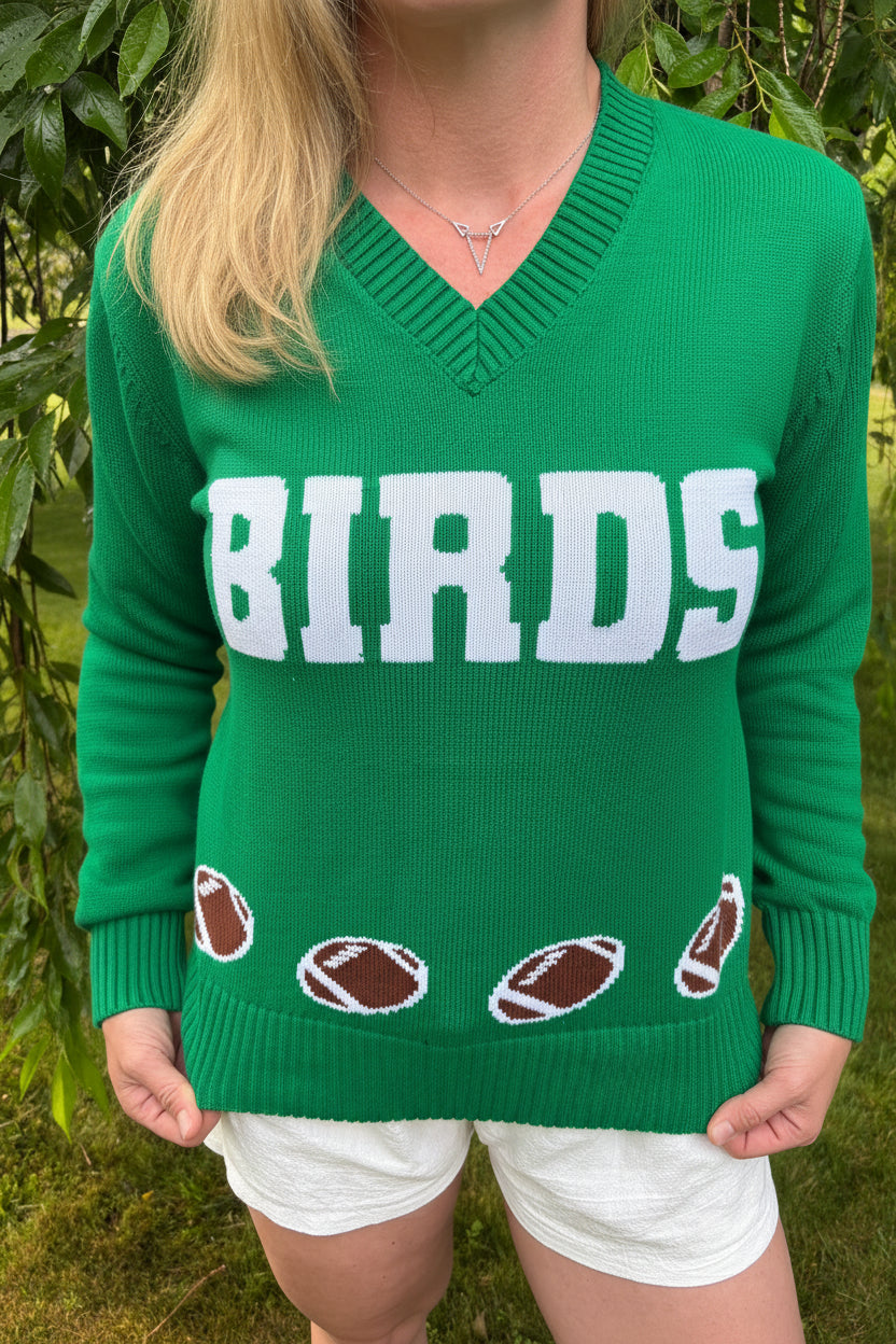 Person wearing a green sweater with 'BIRDS' and football graphics, standing outdoors.